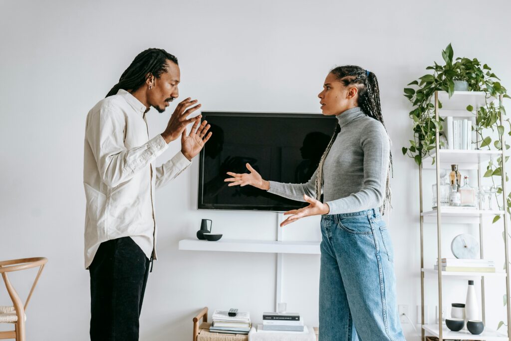 Side view of young African American female in casual outfit gesticulating expressively while arguing with frustrated husband in modern living room