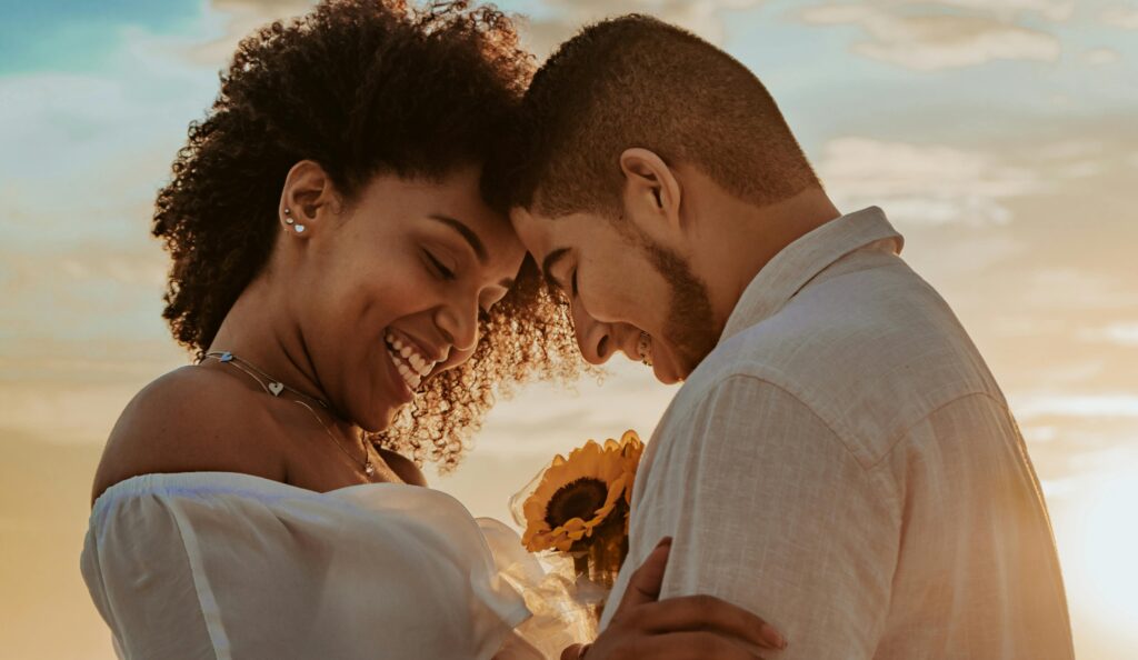 A happy couple lovingly embraces at sunset, holding a sunflower bouquet.